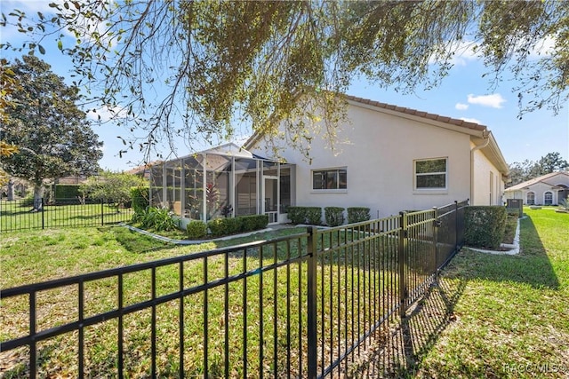 rear view of property featuring glass enclosure, a fenced backyard, a tile roof, a yard, and stucco siding