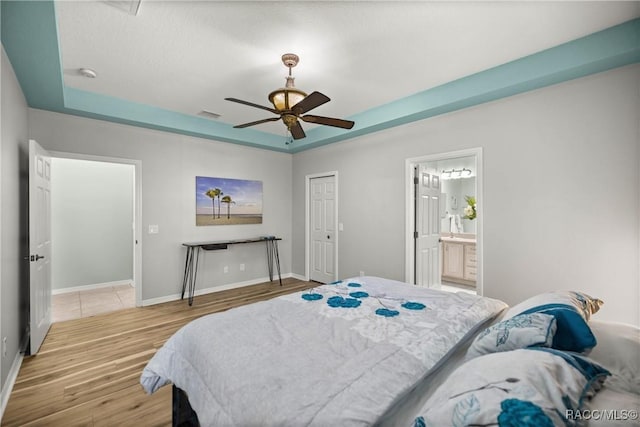 bedroom featuring connected bathroom, wood finished floors, visible vents, baseboards, and a tray ceiling