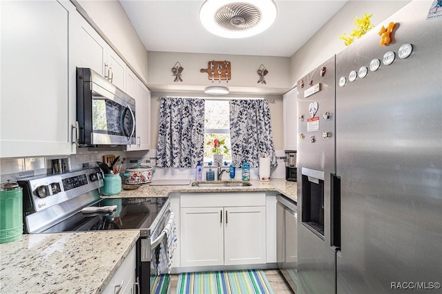 kitchen with appliances with stainless steel finishes, sink, white cabinets, decorative backsplash, and light stone counters