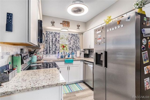 kitchen with sink, white cabinetry, appliances with stainless steel finishes, light stone countertops, and decorative backsplash