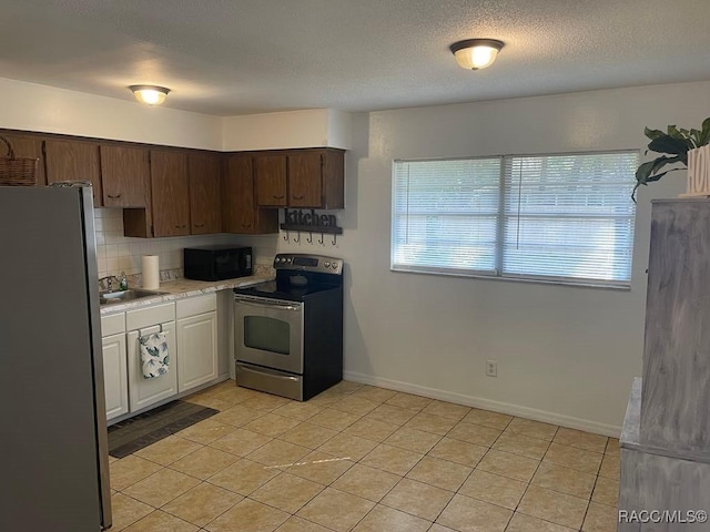 kitchen with light tile patterned flooring, tasteful backsplash, sink, stainless steel appliances, and a textured ceiling