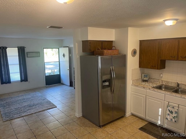 kitchen with light tile patterned flooring, sink, white cabinets, backsplash, and stainless steel refrigerator with ice dispenser