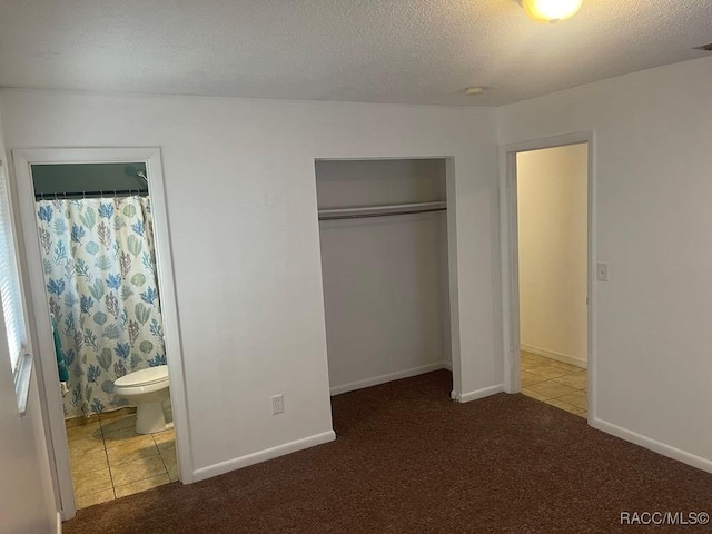 unfurnished bedroom with a closet, ensuite bathroom, carpet, and a textured ceiling