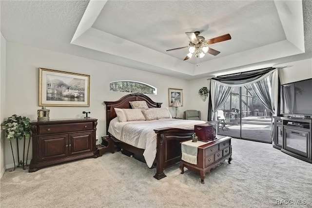 carpeted bedroom with ceiling fan, a raised ceiling, and access to outside