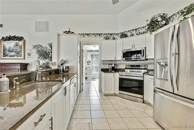 kitchen featuring white cabinetry, sink, dark stone countertops, light tile patterned floors, and appliances with stainless steel finishes