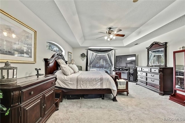 bedroom featuring a textured ceiling, light colored carpet, a raised ceiling, and ceiling fan