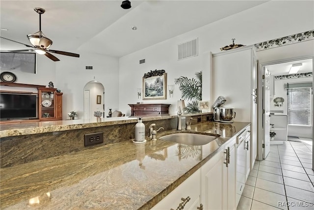 kitchen featuring dark stone counters, white cabinets, sink, vaulted ceiling, and light tile patterned floors