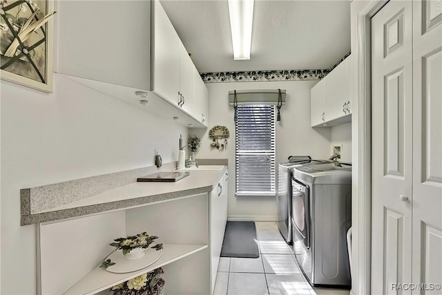 clothes washing area featuring cabinets, light tile patterned floors, and washing machine and clothes dryer