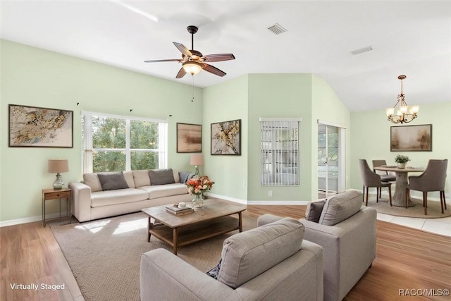 living area with visible vents, light wood-style floors, vaulted ceiling, baseboards, and ceiling fan with notable chandelier