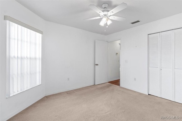 unfurnished bedroom with a ceiling fan, visible vents, a closet, and light colored carpet