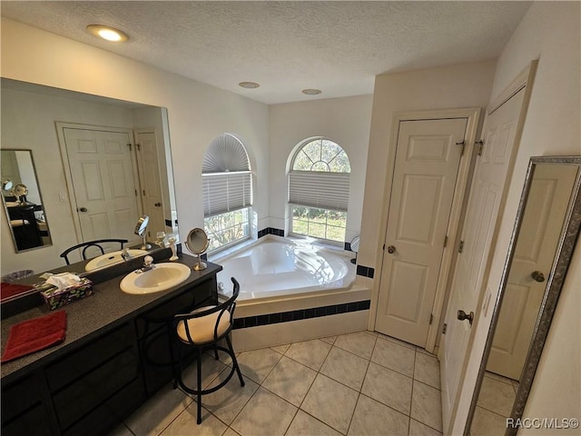 bathroom featuring tile patterned flooring, vanity, tiled tub, and a textured ceiling