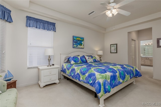 carpeted bedroom featuring ceiling fan, connected bathroom, and a tray ceiling