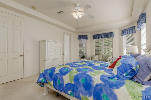 carpeted bedroom featuring ceiling fan, a tray ceiling, and multiple windows