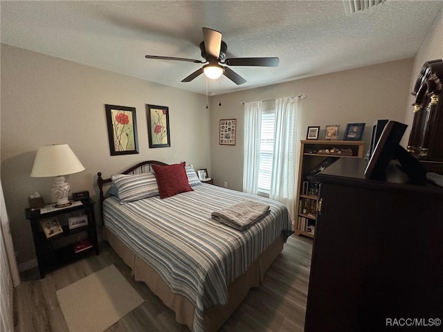 bedroom featuring dark hardwood / wood-style flooring, ceiling fan, and a textured ceiling