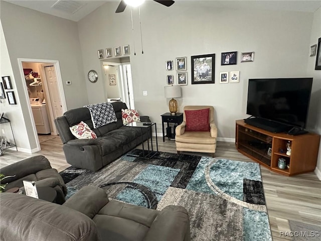 living room featuring washer / clothes dryer, wood-type flooring, high vaulted ceiling, and ceiling fan