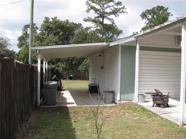 exterior space featuring a carport, an outdoor fire pit, fence, and a patio