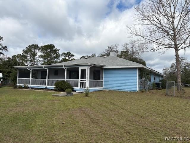 back of house with an attached garage, a sunroom, a chimney, and a yard