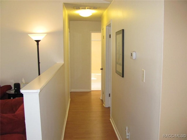 hall featuring an upstairs landing, wood finished floors, visible vents, and baseboards