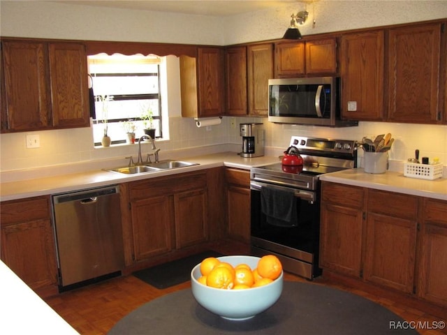 kitchen featuring brown cabinetry, stainless steel appliances, a sink, and light countertops