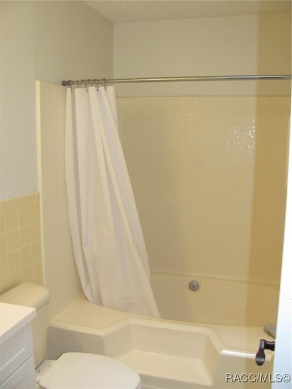 full bathroom with toilet, shower / bath combination with curtain, vanity, and tile walls