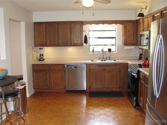 kitchen with brown cabinets, light countertops, appliances with stainless steel finishes, a sink, and ceiling fan