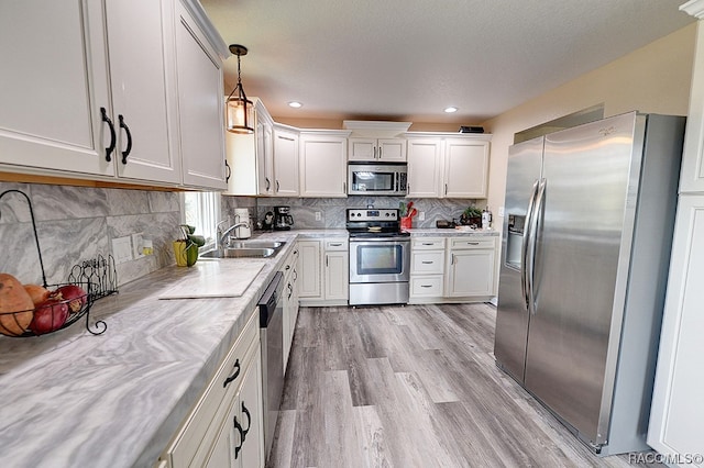 kitchen with sink, hanging light fixtures, light hardwood / wood-style flooring, white cabinetry, and stainless steel appliances