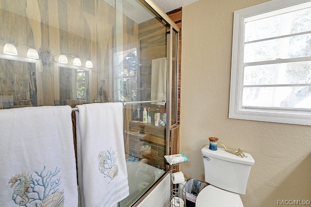 bathroom featuring toilet, bath / shower combo with glass door, and a wealth of natural light