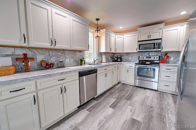 kitchen featuring pendant lighting, white cabinets, stainless steel appliances, and light hardwood / wood-style flooring