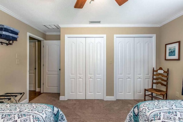 carpeted bedroom with multiple closets, ornamental molding, and ceiling fan