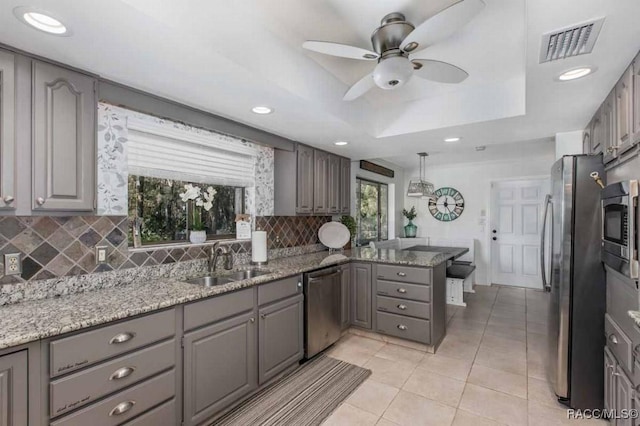 kitchen with sink, gray cabinetry, stainless steel appliances, a tray ceiling, and kitchen peninsula