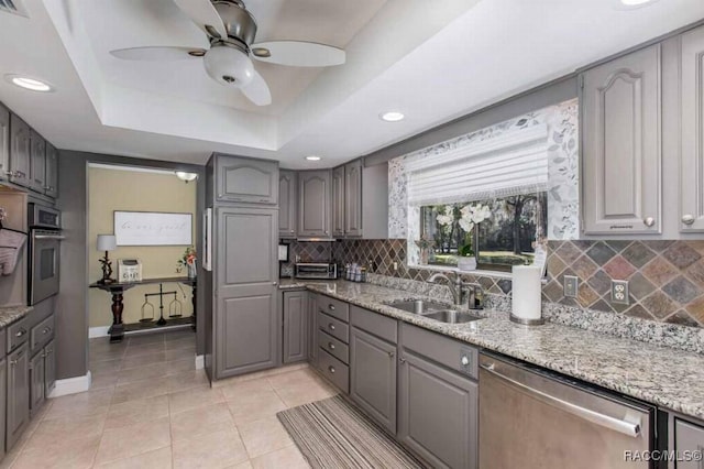 kitchen featuring sink, gray cabinetry, light stone counters, appliances with stainless steel finishes, and a raised ceiling