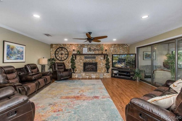 living room featuring hardwood / wood-style flooring, a stone fireplace, ornamental molding, and ceiling fan