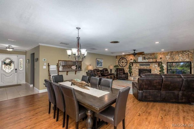 dining area with crown molding, a fireplace, ceiling fan with notable chandelier, and light wood-type flooring