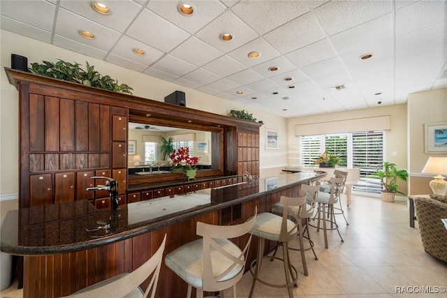 bar with a paneled ceiling, sink, and dark stone counters