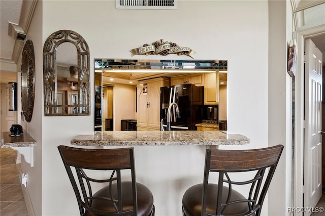 kitchen featuring a kitchen bar, kitchen peninsula, light stone countertops, black fridge with ice dispenser, and tile patterned flooring