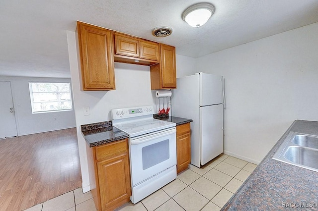 kitchen with visible vents, brown cabinets, a sink, white appliances, and light tile patterned floors