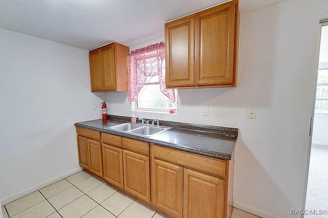 kitchen with light tile patterned floors, brown cabinetry, baseboards, a sink, and dark countertops