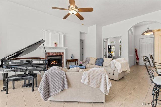 living room with a ceiling fan, arched walkways, light tile patterned floors, and a premium fireplace