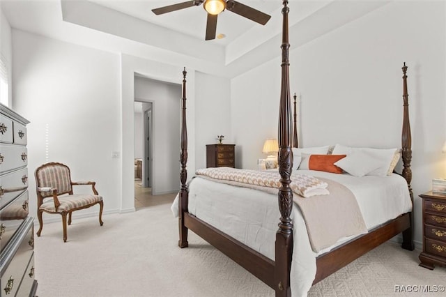 bedroom with a raised ceiling, a ceiling fan, and light colored carpet