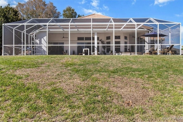 rear view of house with a lawn, a lanai, and a ceiling fan