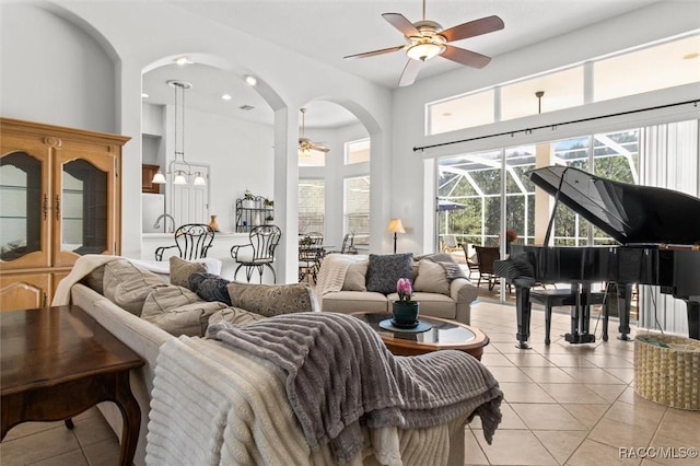 living area with a ceiling fan, a sunroom, a towering ceiling, and light tile patterned floors