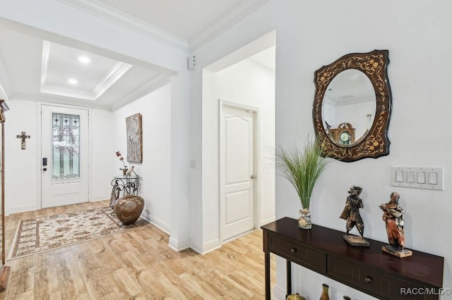 foyer featuring light wood-style floors, baseboards, a raised ceiling, and crown molding