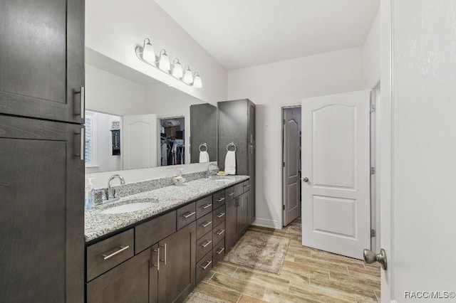 full bathroom featuring baseboards, double vanity, a sink, and wood tiled floor