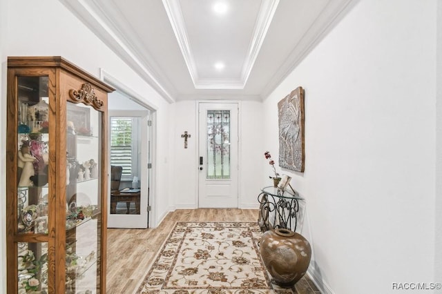 foyer with light wood-type flooring, baseboards, crown molding, and a tray ceiling