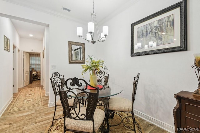 dining room featuring visible vents, baseboards, light wood-style floors, an inviting chandelier, and crown molding