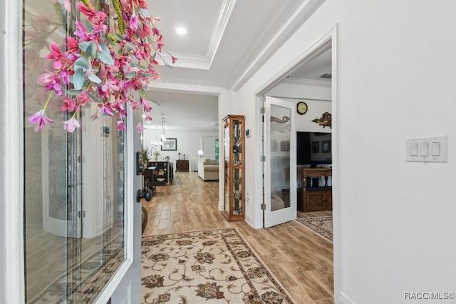 foyer entrance with light wood finished floors, a tray ceiling, crown molding, and french doors