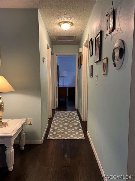 hall with a textured ceiling and dark wood-type flooring