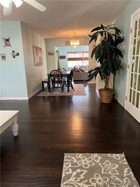 dining area featuring ceiling fan with notable chandelier, dark wood-type flooring, and a textured ceiling