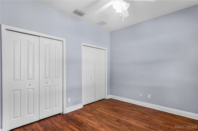 unfurnished bedroom featuring multiple closets, ceiling fan, and dark hardwood / wood-style flooring