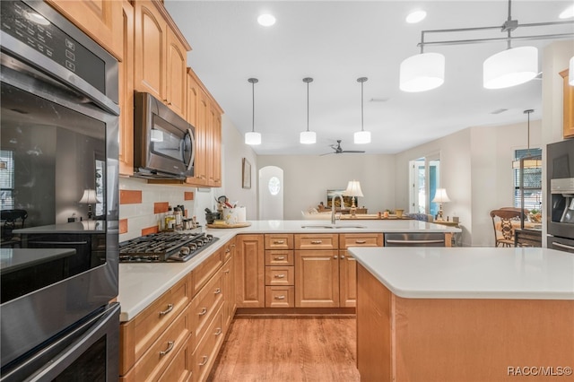 kitchen featuring pendant lighting, sink, stainless steel appliances, a kitchen island, and light wood-type flooring